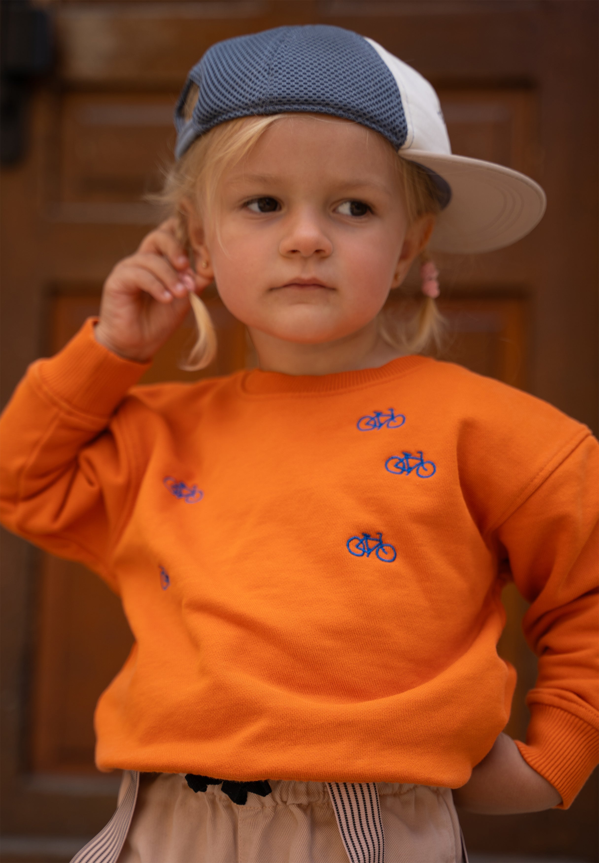 Child wearing orange organic cotton sweatshirt with embroidered bicycle design