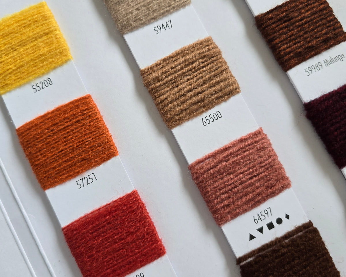 A close-up of a fabric or yarn color swatch card displaying multiple vertical color options, including cream, yellow, orange, red, pink, brown, and dark maroon, each labeled with a shade number.
