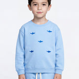 A young boy wearing a light blue Slopes and Town kids sweatshirt and matching sweatpants set, featuring a pattern of small dark blue shark silhouettes