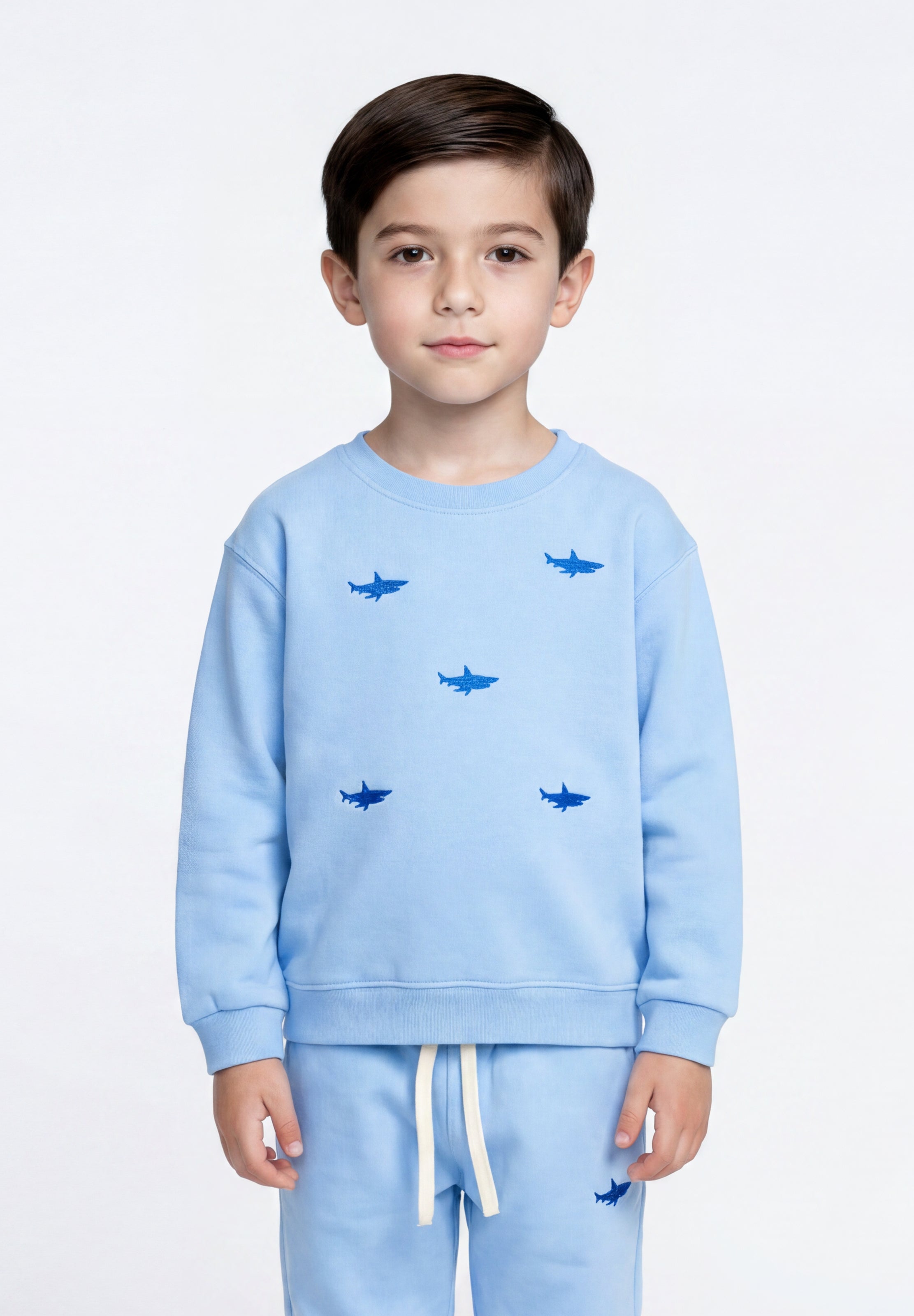 A young boy wearing a light blue Slopes and Town kids sweatshirt and matching sweatpants set, featuring a pattern of small dark blue shark silhouettes