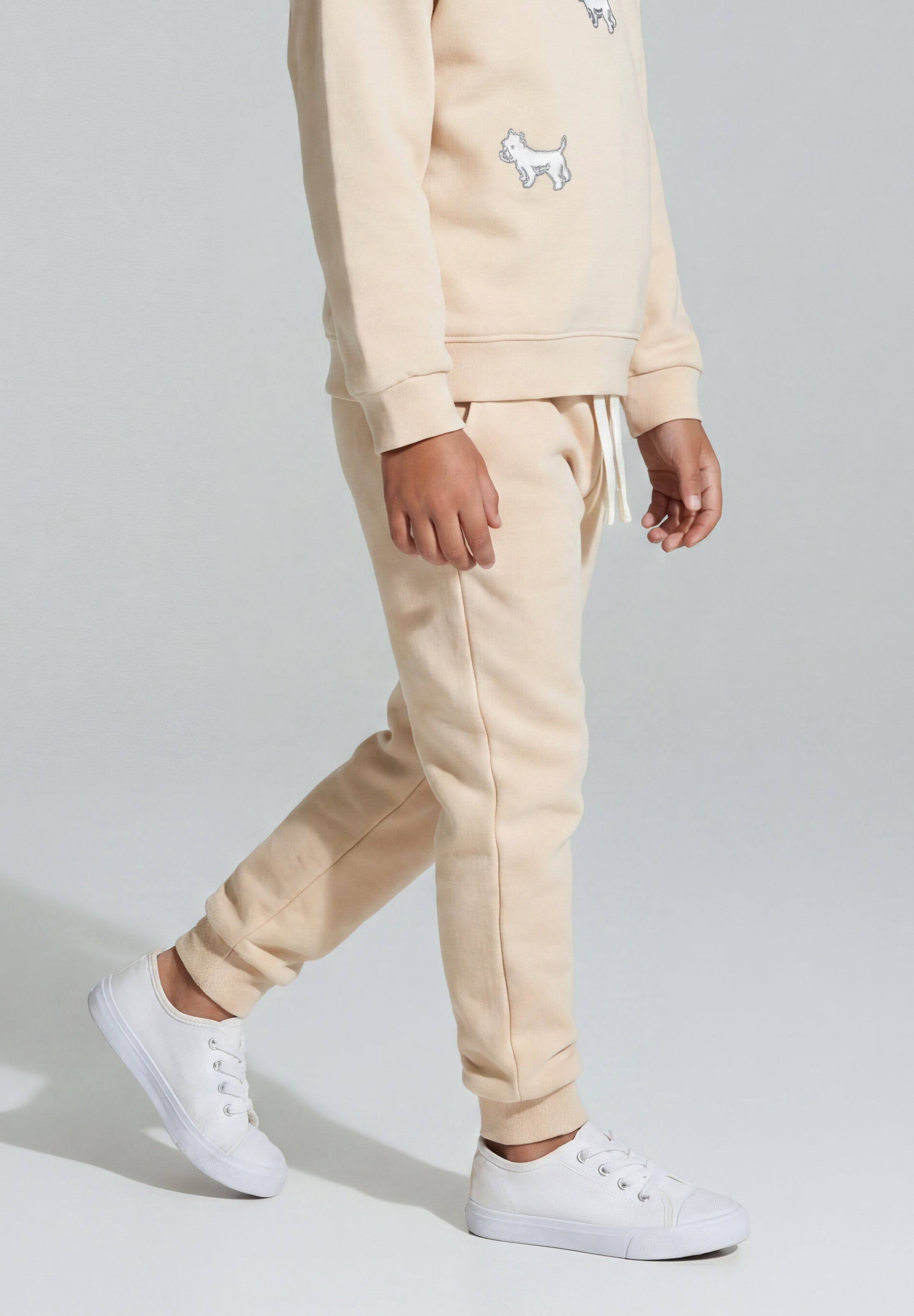 Child wearing beige sweatpants with white terrier dog embroidery