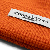 Close-up of Slopes and Town Amsterdam woven label on orange kids merino wool beanie