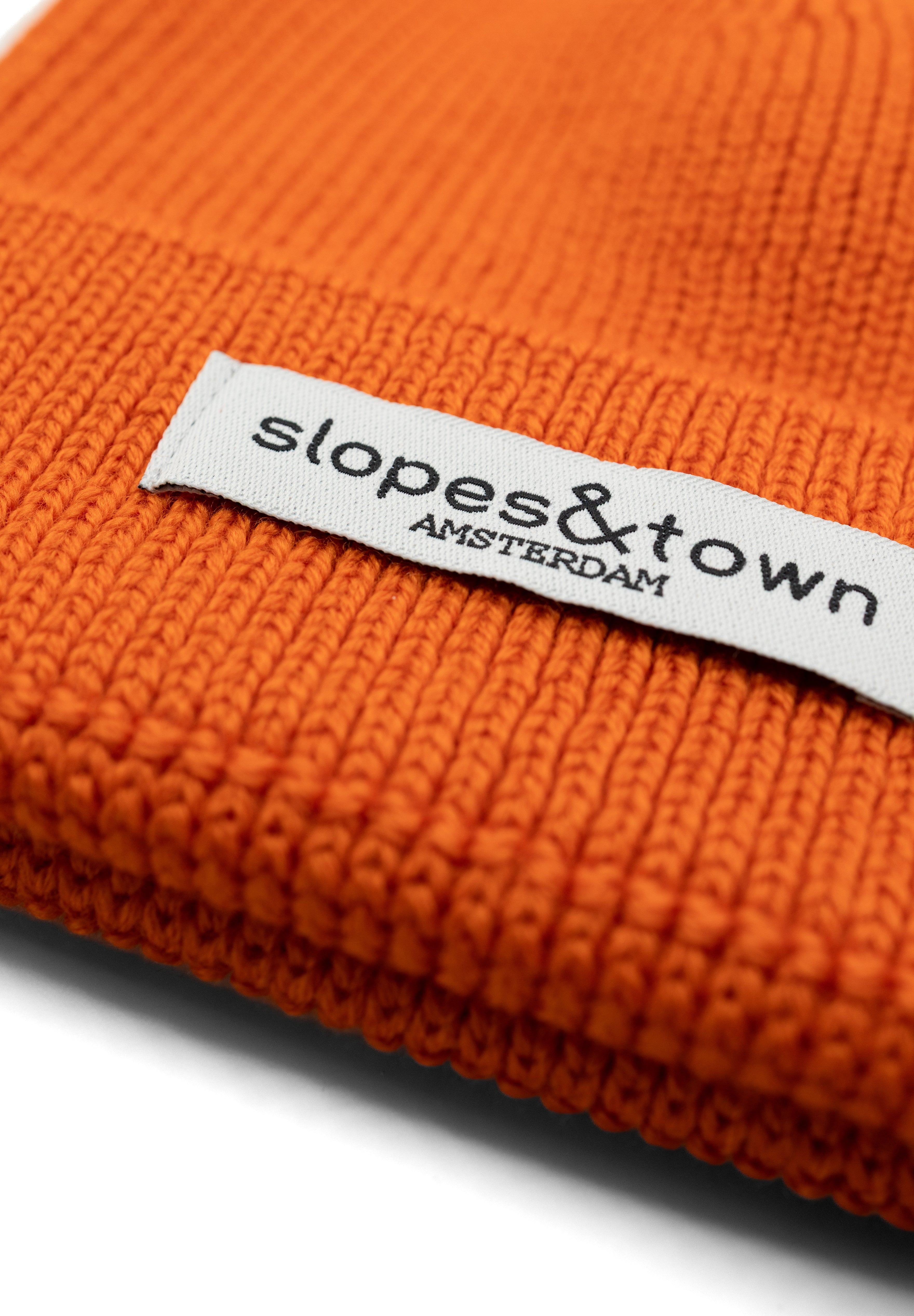 Close-up of Slopes and Town Amsterdam woven label on orange kids merino wool beanie