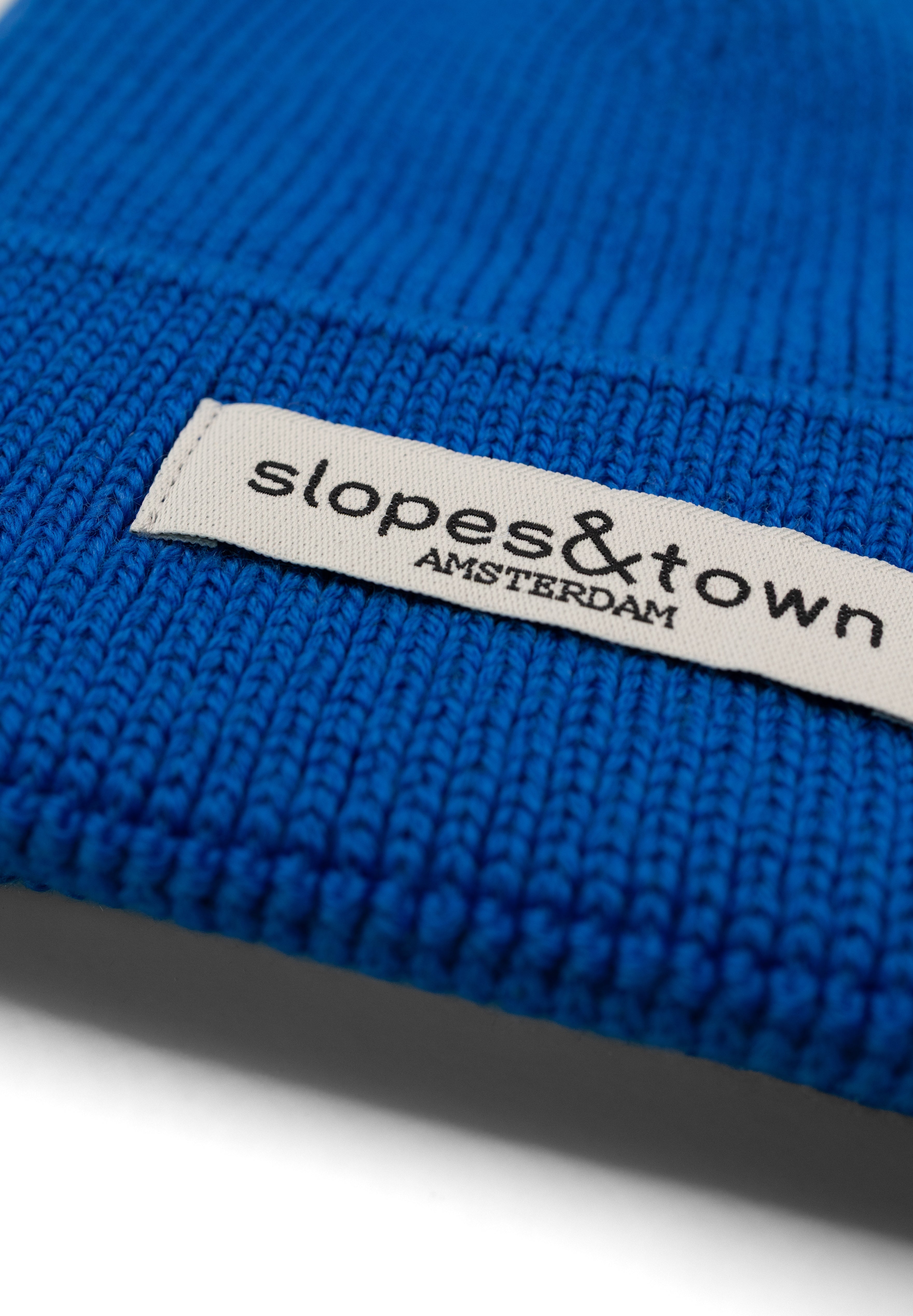 Close-up of Slopes and Town Amsterdam woven label on electric blue kids merino wool beanie