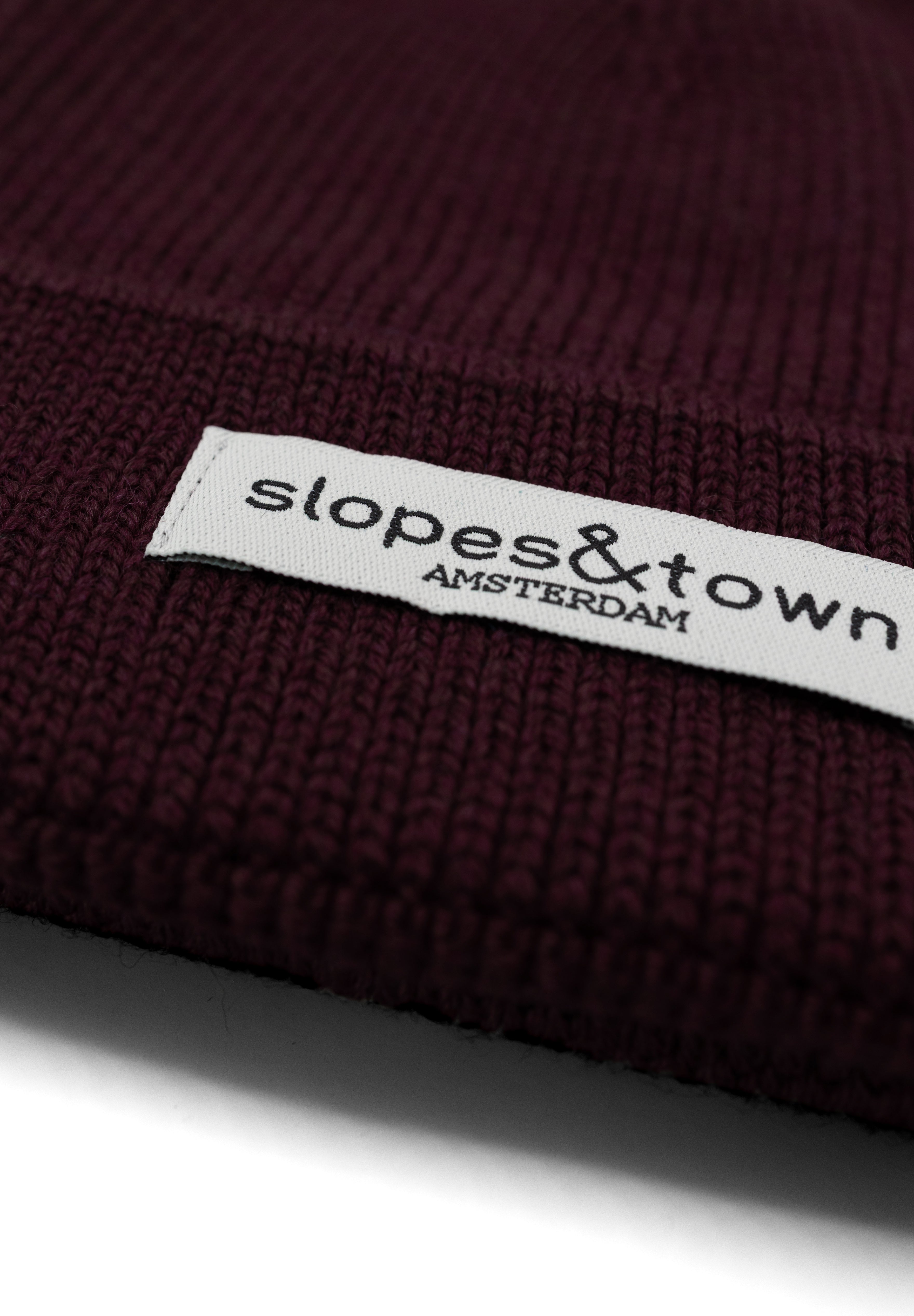 Close-up of Slopes and Town Amsterdam woven label on burgundy kids merino wool beanie