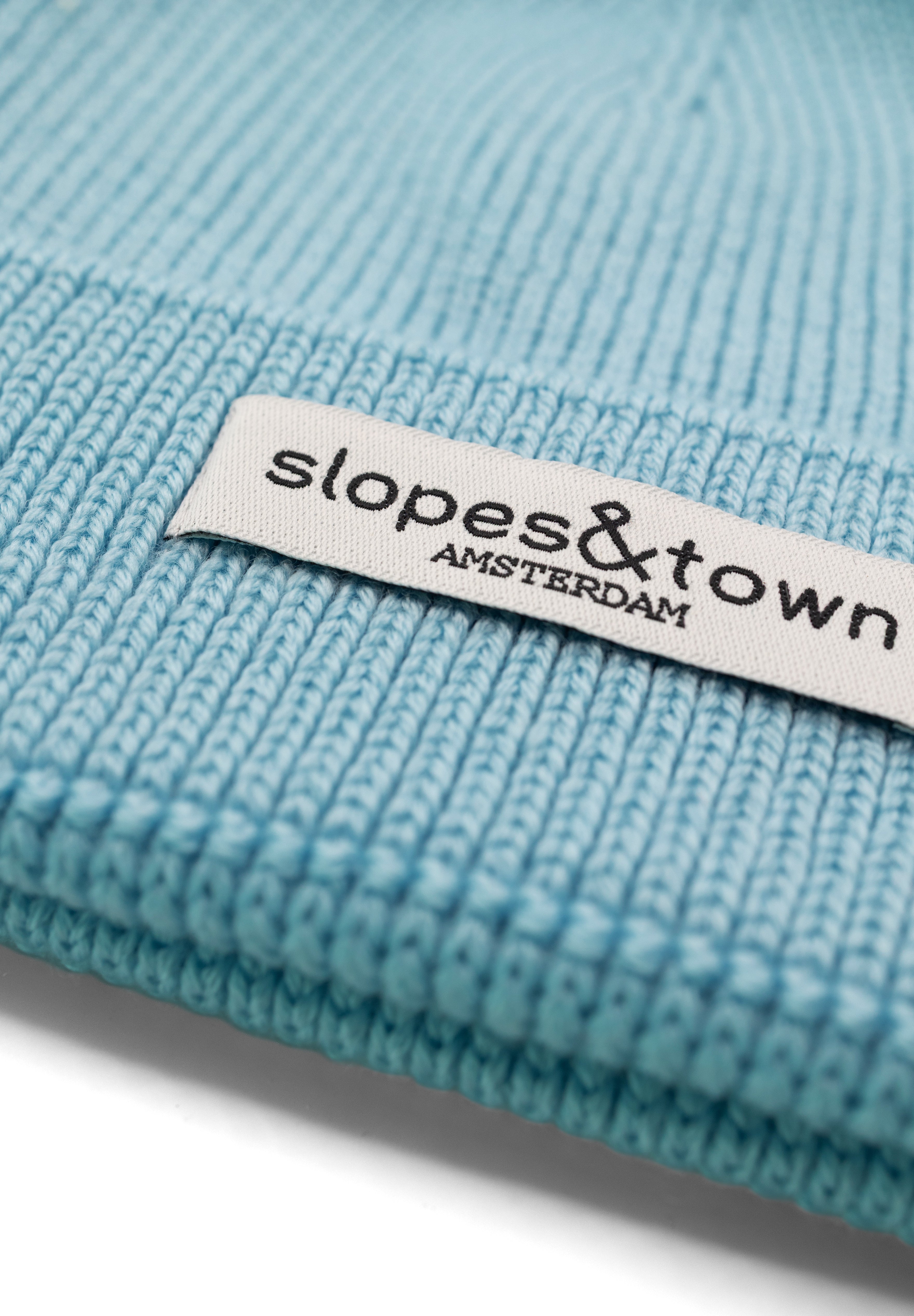 Close-up of Slopes and Town Amsterdam woven label on light blue kids merino wool beanie