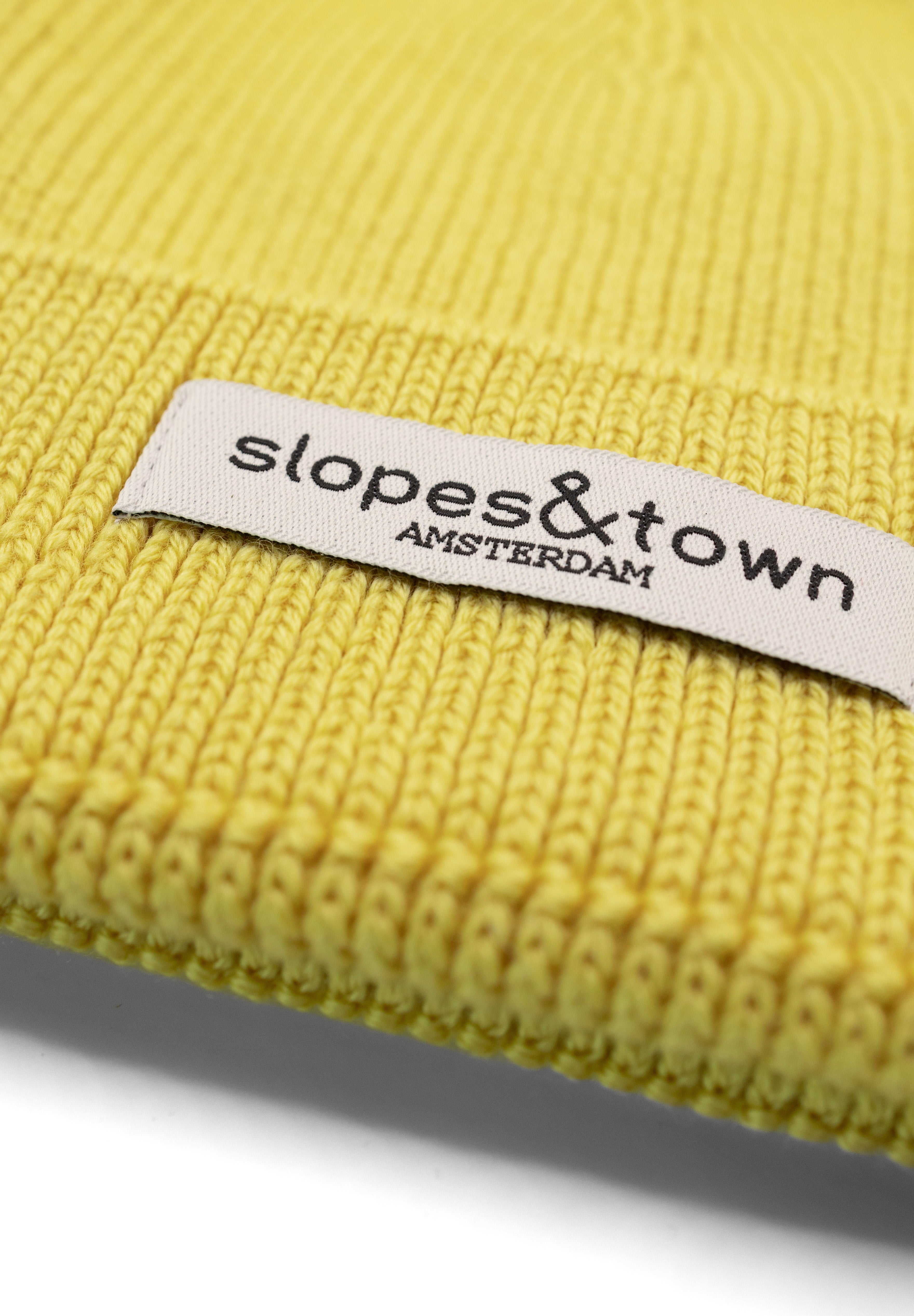 Close-up of Slopes and Town Amsterdam woven label on yellow  kids merino wool beanie