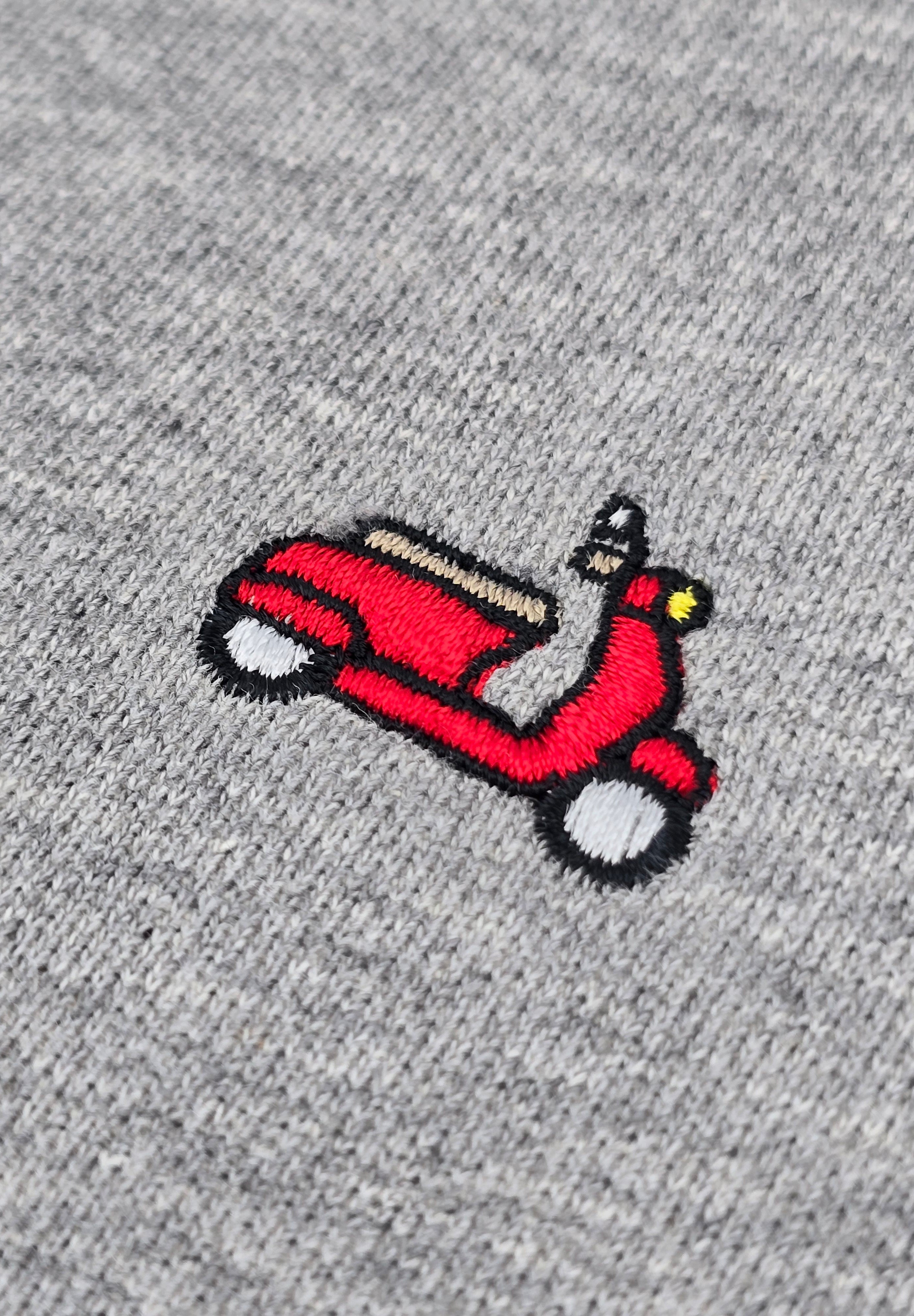 Close-up of a red embroidered vespa patch on a heather gray knit fabric background.