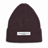 A dark brown ribbed knit beanie hat with a white rectangular brand patch on the front cuff that reads 'slopes&town AMSTERDAM'.