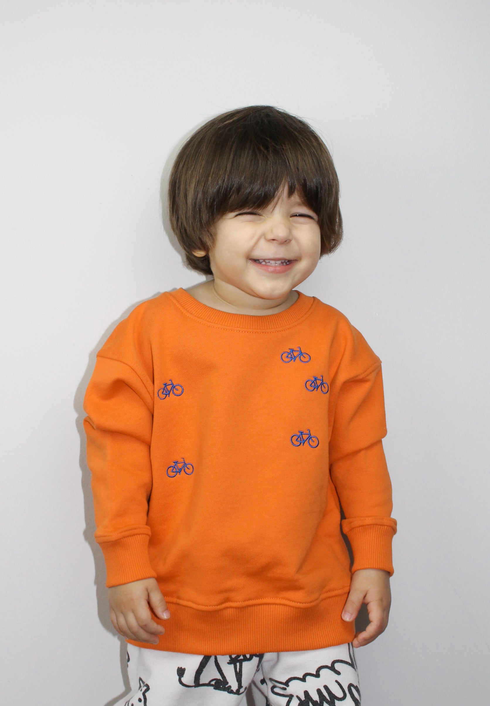A boy wearing orange organic cotton sweatshirt with embroidered bicycle design
