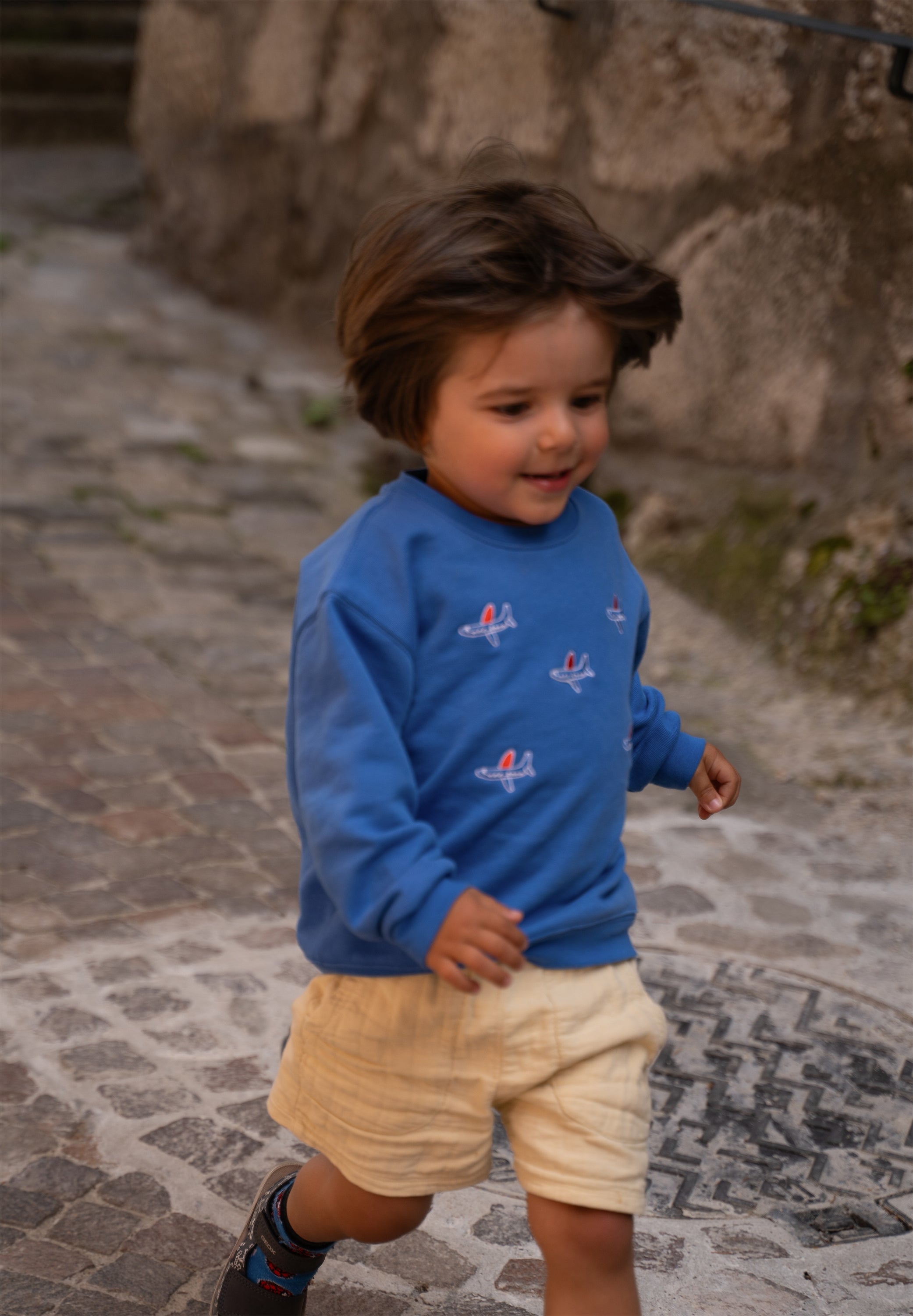 Child wearing blue organic cotton sweatshirt with airplane embroidery