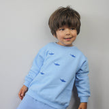 Child wearing blue tracksuit top with embroidered shark design