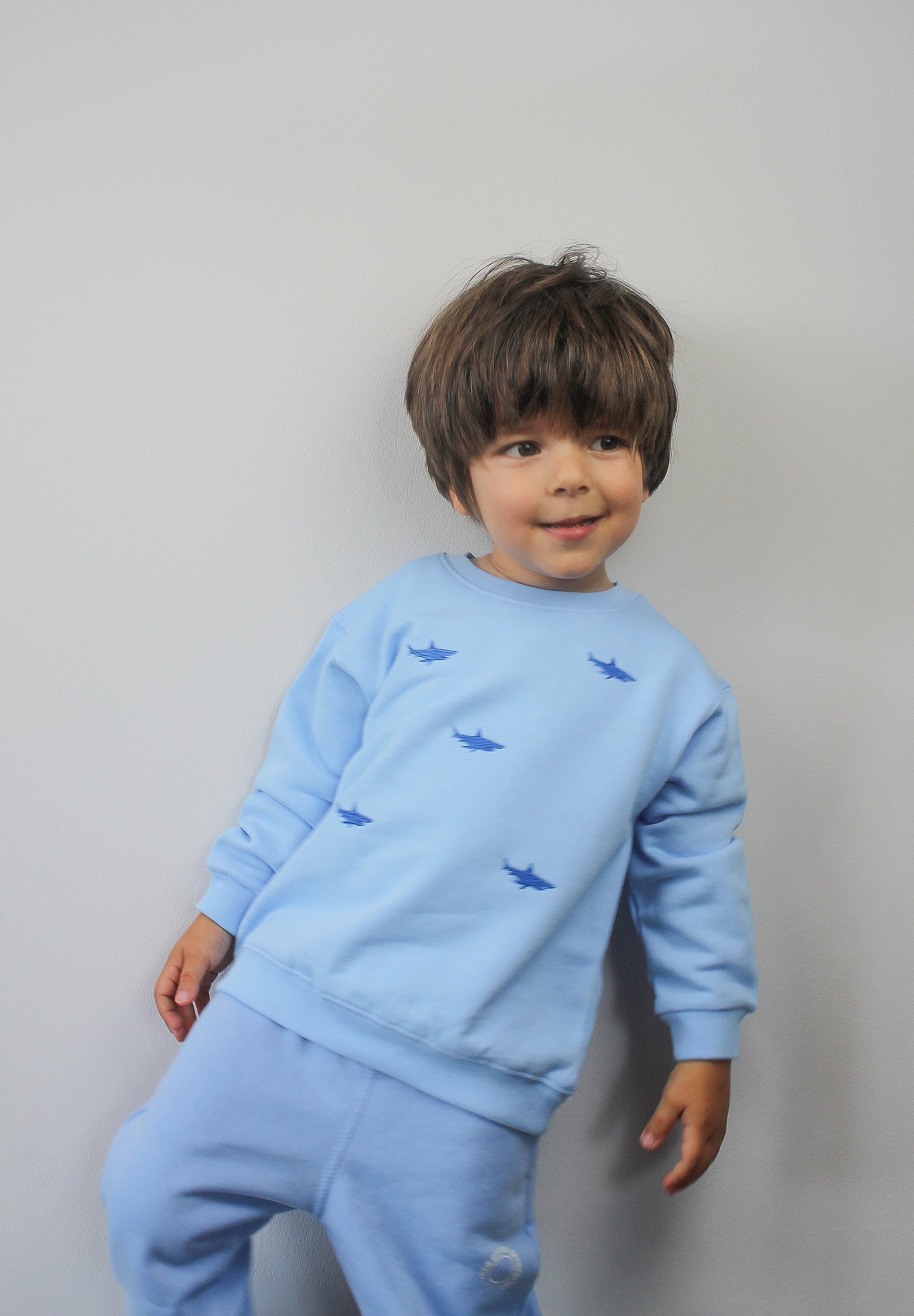 Child wearing blue tracksuit top with embroidered shark design