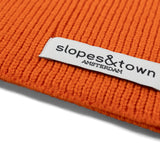 Close-up of Slopes and Town Amsterdam woven label on orange kids merino wool snood