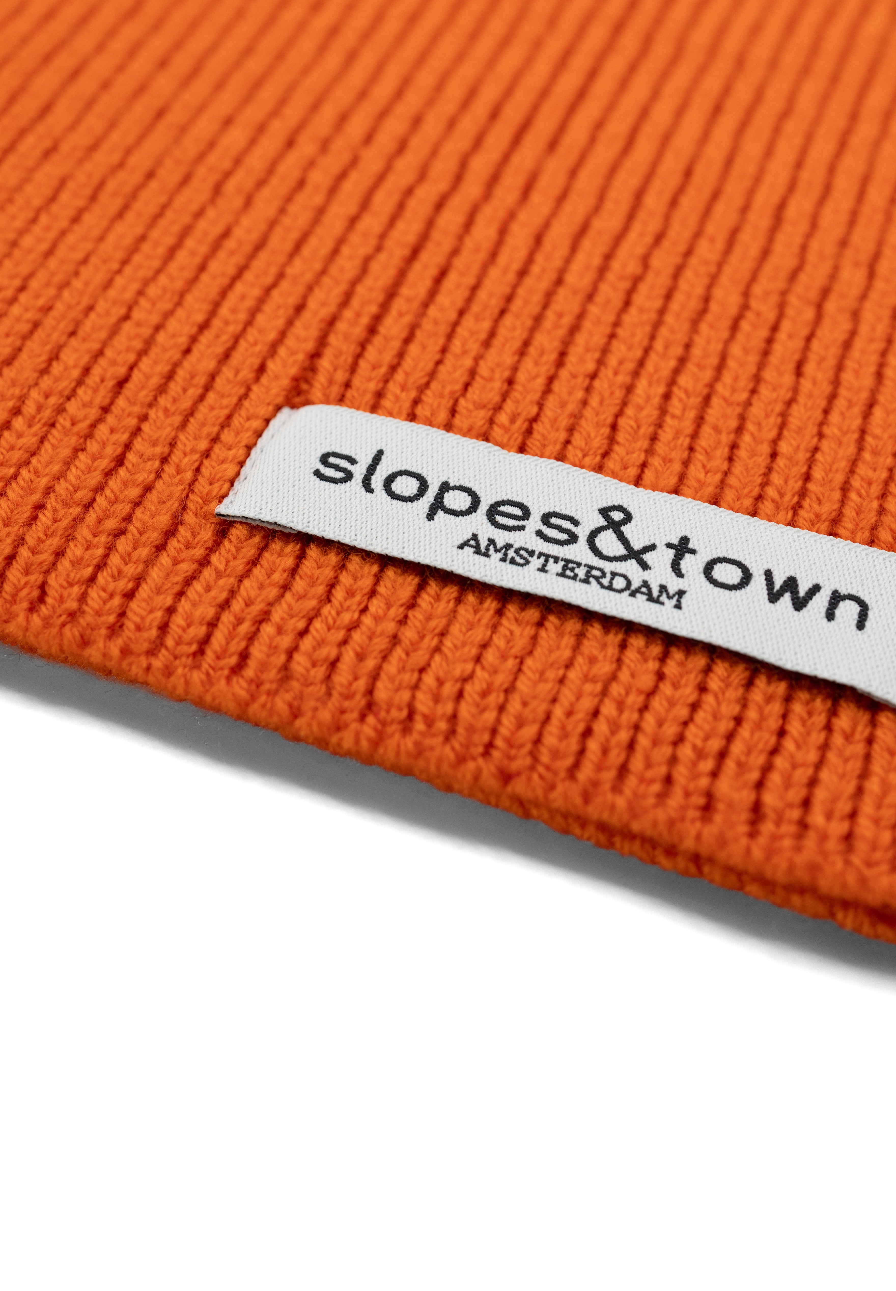 Close-up of Slopes and Town Amsterdam woven label on orange kids merino wool snood