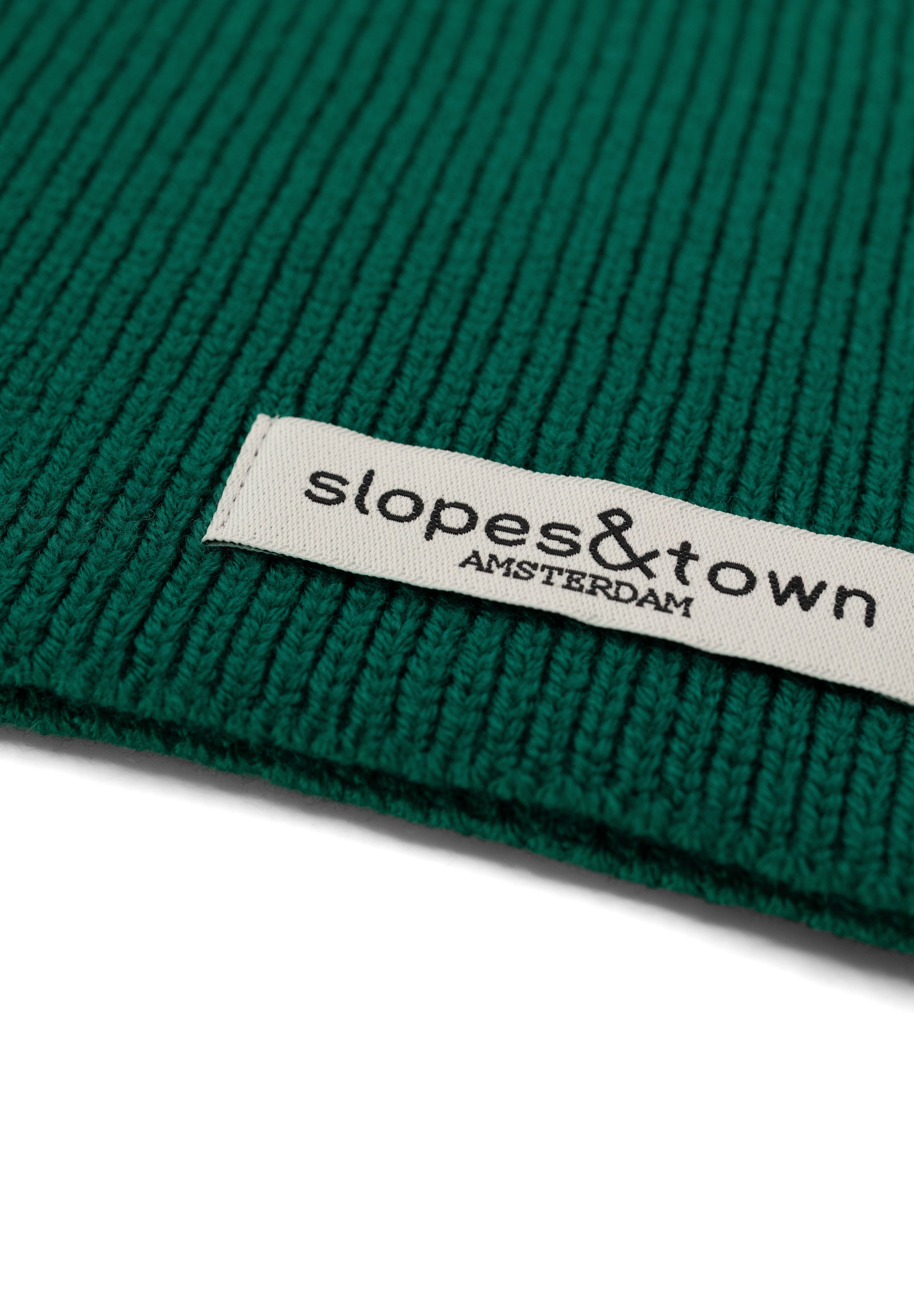 Close-up of Slopes and Town Amsterdam woven label on pine green kids merino wool snood