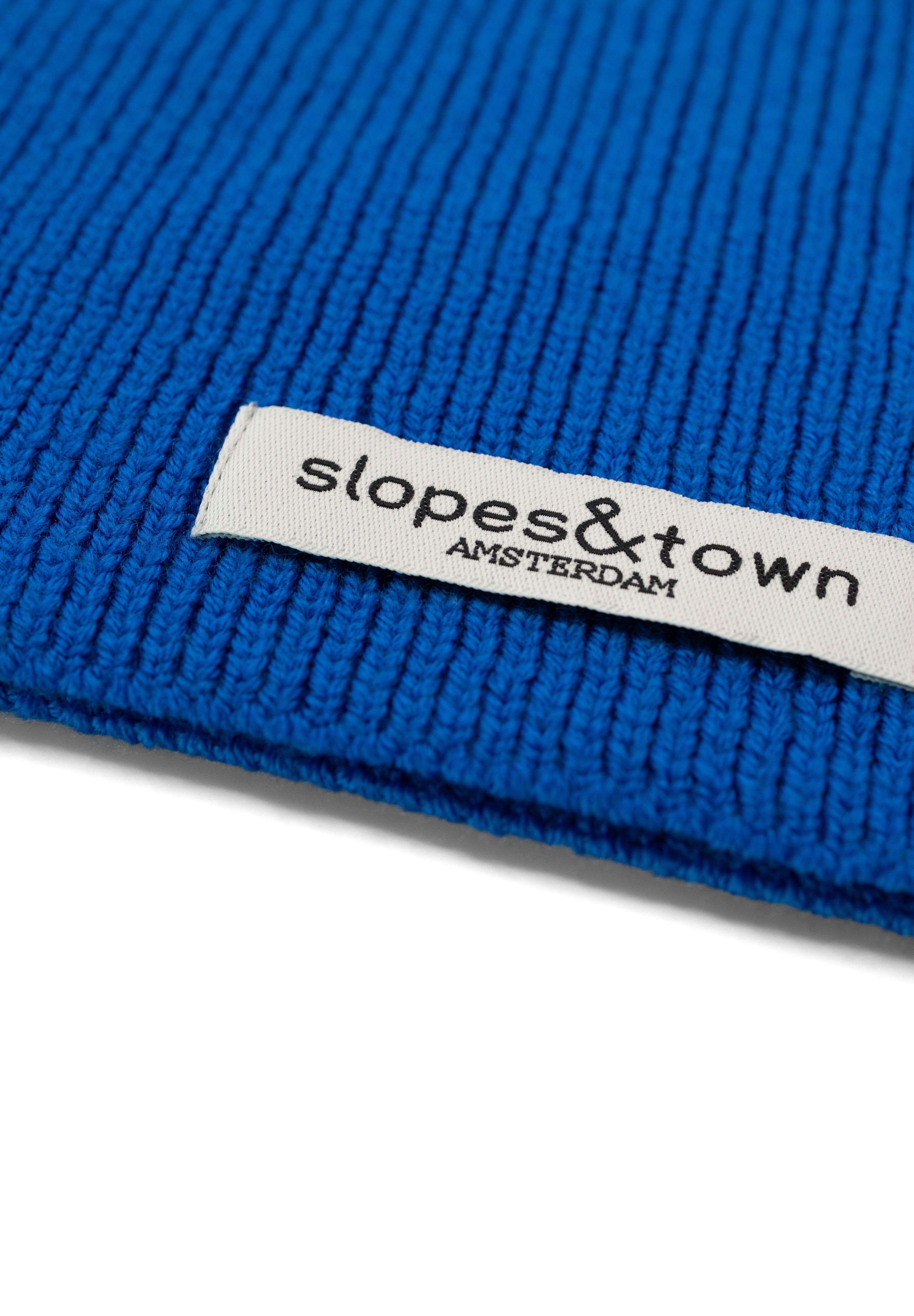 Close-up of Slopes and Town Amsterdam woven label on electric blue kids merino wool snood