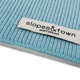 Close-up of Slopes and Town Amsterdam woven label on light blue kids merino wool snood