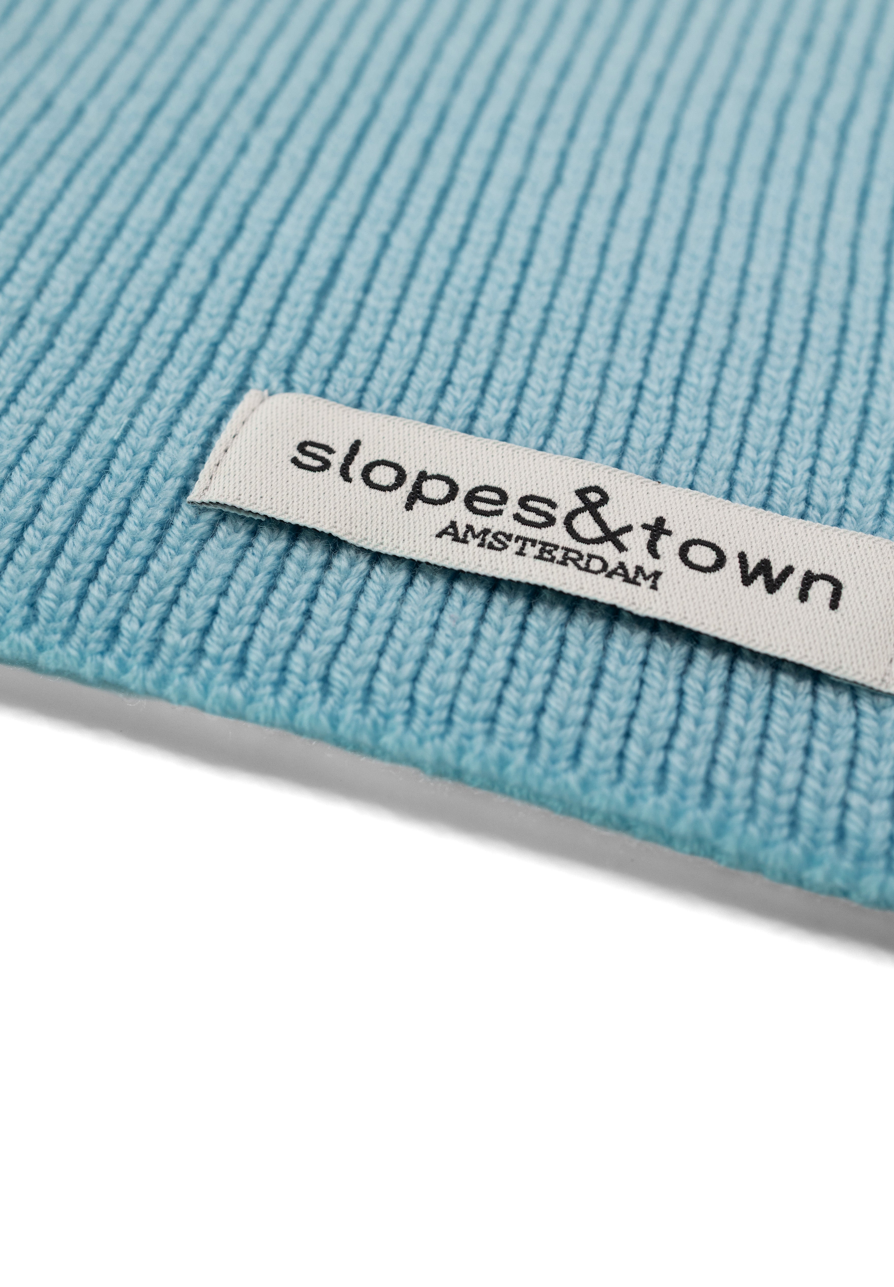 Close-up of Slopes and Town Amsterdam woven label on light blue kids merino wool snood