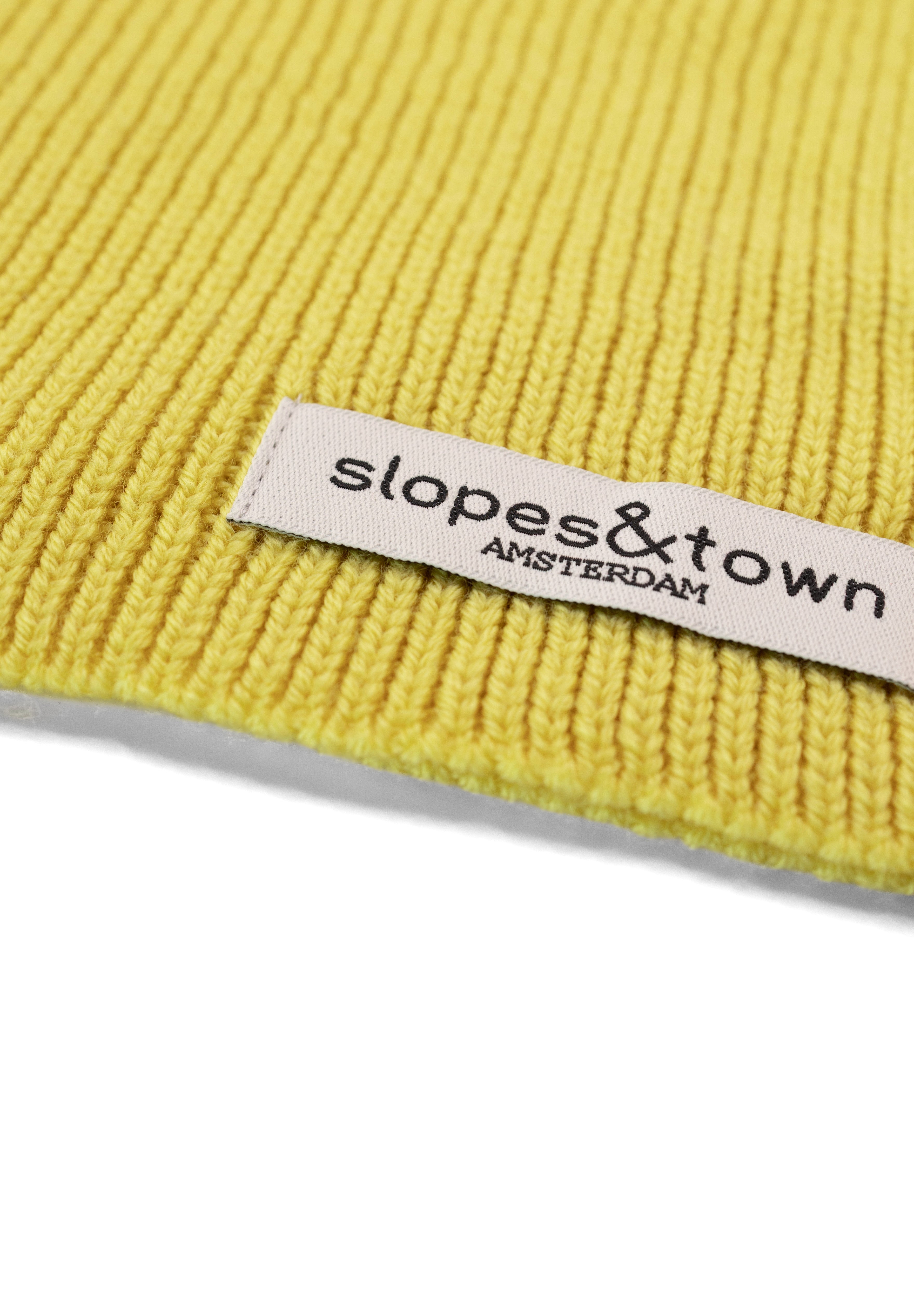Close-up of Slopes and Town Amsterdam woven label on yellow kids merino wool snood